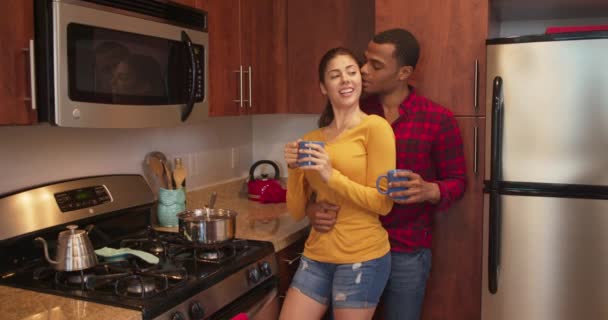 Millennial ζευγάρι πίνοντας πρωινό καφέ και παιχνιδιάρικα φιλιά στην κουζίνα. Αφρο-αμερικάνος κρατάει την κοπέλα του κοντά. 4k αργής κίνησης χειρός - Πλάνα, βίντεο