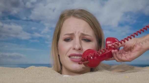 Una bella donna sepolta fino alla testa su una spiaggia che riceve notizie inquietanti su un telefono rosso - Filmati, video