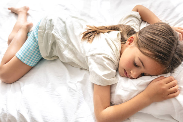 Una linda niña en pijama duerme dulcemente en la cama. - Foto, imagen