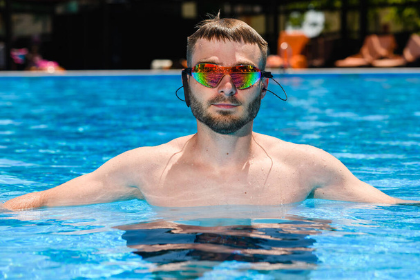 Professional male swimmer in goggles glasses in swimming pool, sportsman portrait at water surface, active weekend, vacation - Fotografie, Obrázek