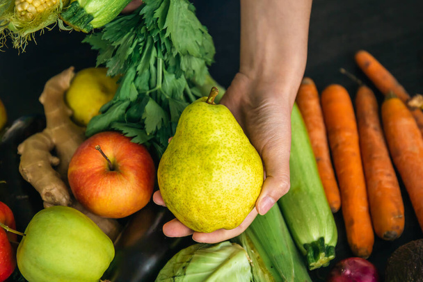 Großaufnahme, eine Birne in weiblicher Hand auf verschwommenem Hintergrund mit Gemüse, dem Konzept von Ernährung und Gesundheit. - Foto, Bild