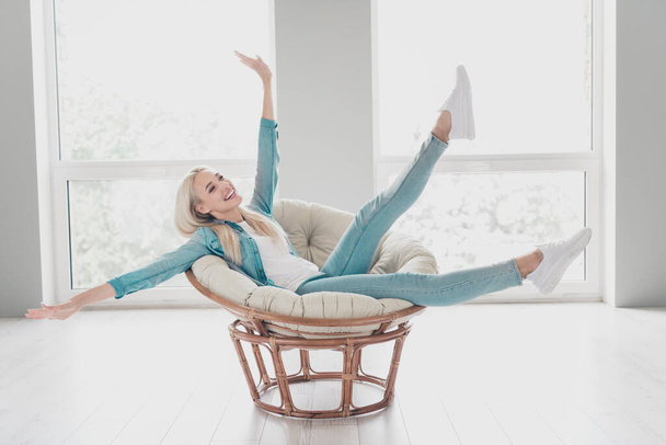Photo of charming sweet young girl wear jeans shirt sitting chair smiling hands arms sides having rest indoors house room. - Фото, зображення