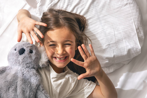 Cute little girl with favorite soft toy in bed smiling in the morning. - Photo, Image