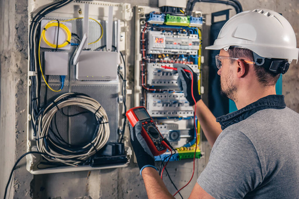 Man, an electrical technician working in a switchboard with fuses. Installation and connection of electrical equipment. Professional uses a tablet. - 写真・画像