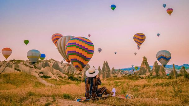 Asian women watching the sunset in Cappadocia with hot air balloons in the sky during sunrise in Cappadocia Turkey. Kapadokya Gorem. Happy mid age women in a hot air balloon  - Photo, Image