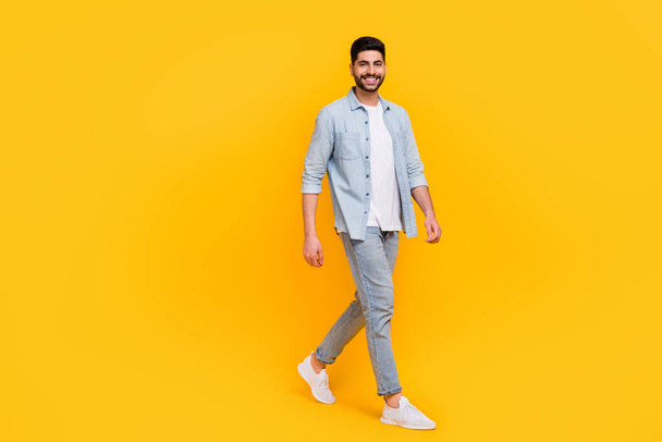 Full size photo of handsome latin guy walking toothy beaming enjoy free time wear stylish jeans outfit isolated on yellow color background. - Fotó, kép