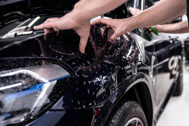 Mitarbeiter des Autodetailstudios schützt den Kotflügel des Autos mit einer farblosen Schutzfolie vor Beschädigungen, Kratzern und Ausbleichen unter dem Einfluss von UV-Strahlung - Foto, Bild