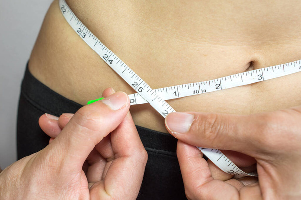 Close-up of woman measuring her waist by measure tape. - Φωτογραφία, εικόνα