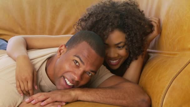 Afroamerykańska para śmiejąca się i leżąca na kanapie - Materiał filmowy, wideo