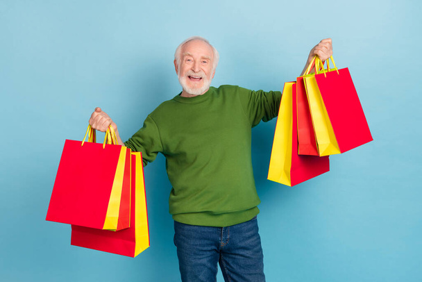 Portrait of excited cheerful granddad hold boutique packages toothy smile isolated on blue color background. - Φωτογραφία, εικόνα