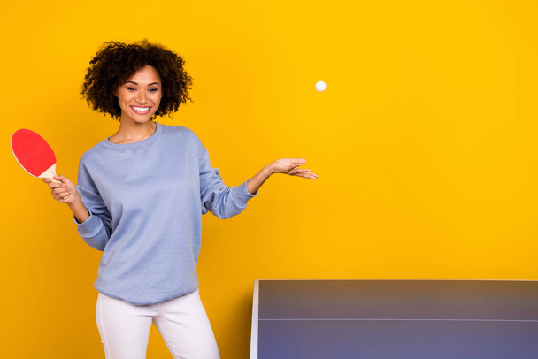 Photo of funny cute curly girl dressed blue pullover throwing ball playing table tennis isolated yellow color background. - Fotó, kép