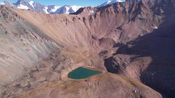 Bir dağ gölünün sularının zümrüt rengi. Dağların yansıması olan yeşil bir dağ gölünün drone görüntüsü. Pürüzsüz şeffaf su. Yakınlarda büyük taşlar var. Kuru çimler Kazakistan - Video, Çekim