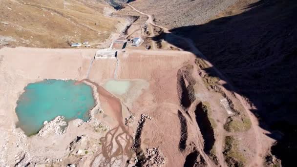 A mountain artificial lake with blue water and a dam. The turquoise surface of the water reflects the mountains. There is a small lake with muddy water nearby. Self-protective dam in the mountains - Footage, Video