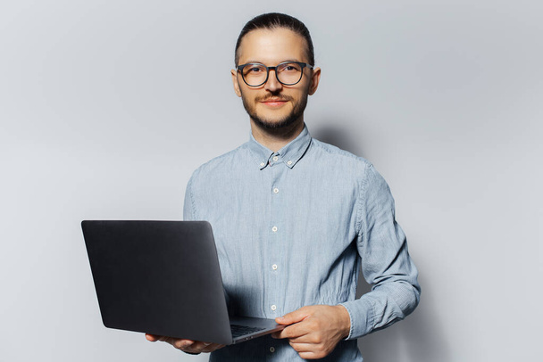 Studio portret van jonge serieuze man met een laptop in de hand, het dragen van een blauw shirt en een bril op een witte achtergrond. - Foto, afbeelding
