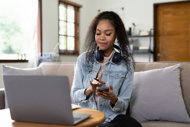 Junge Frau benutzt Handy beim Online-Lernen mit Laptop zu Hause - Foto, Bild