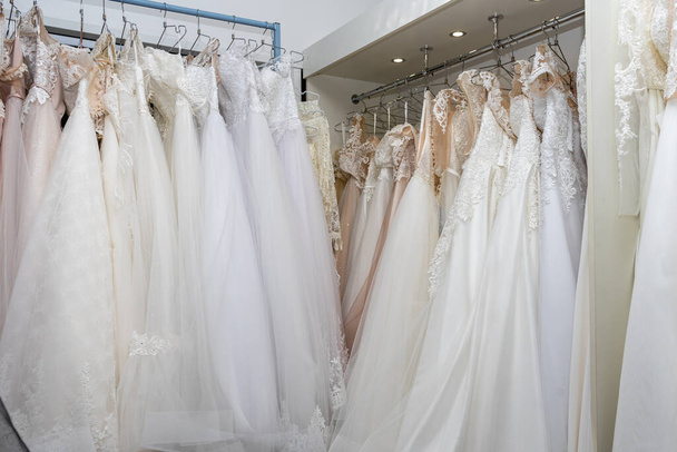 White and cream wedding dresses on a hanger in a bridal boutique. Close up. - 写真・画像