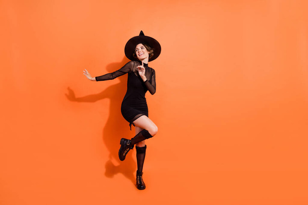Full size photo of nice young woman dance look empty space dressed trendy black halloween witch garment isolated on orange color background. - Foto, imagen