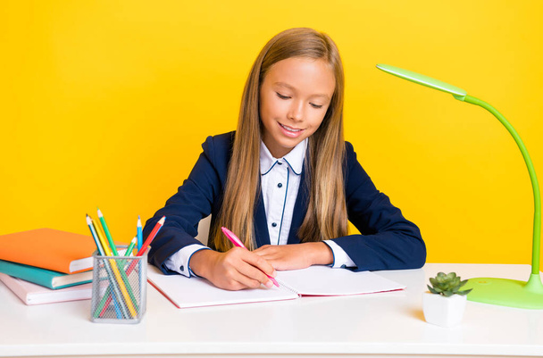 Portrait of positive intelligent girl learner sit table look notebook write essay distance home study isolated on yellow color background. - 写真・画像