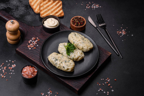 Традиционные литовские дирижабли, вареные картофельные пельмени, фаршированные мясом, на черной керамической пластине на темно-бетонном фоне - Фото, изображение