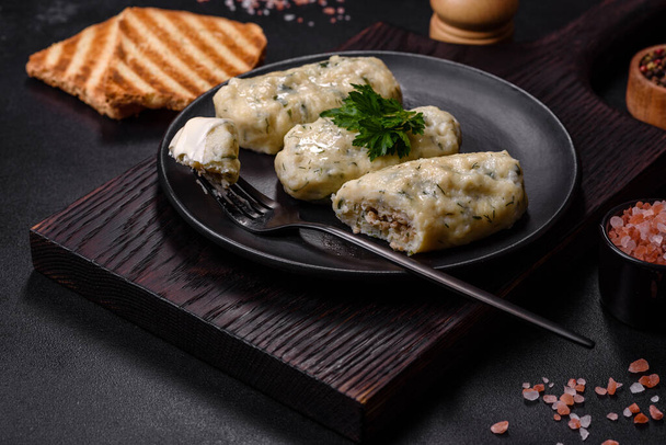 Traditional Lithuanian dish zeppelin, boiled potato dumplings stuffed with minced meat, on a black ceramic plate on a dark concrete background - Photo, Image