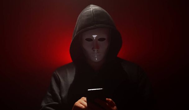 Ο άνθρωπος φορώντας μάσκα με κουκούλα εκτοξεύει τον ιό από το smartphone. - Φωτογραφία, εικόνα