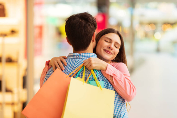 Mari embrassant femme faisant du shopping ensemble posant tenant sacs Shopper debout dans l'hypermarché moderne, l'achat de vêtements neufs le week-end. Shopaholism et offre de vente. Focus sélectif - Photo, image