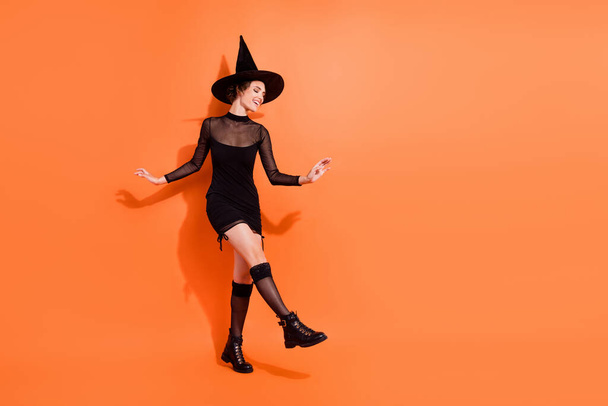 Full length photo of winsome young lady discotheque clubbing wear stylish black halloween witch look isolated on orange color background. - Fotografie, Obrázek