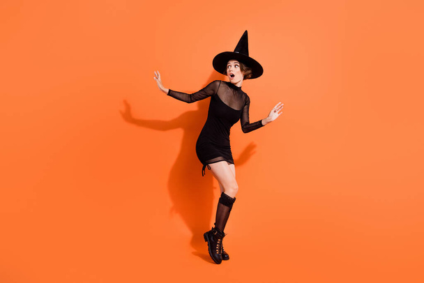 Full body photo of cute girl look frighten empty space escape dressed trendy black halloween garment isolated on orange color background. - Fotoğraf, Görsel