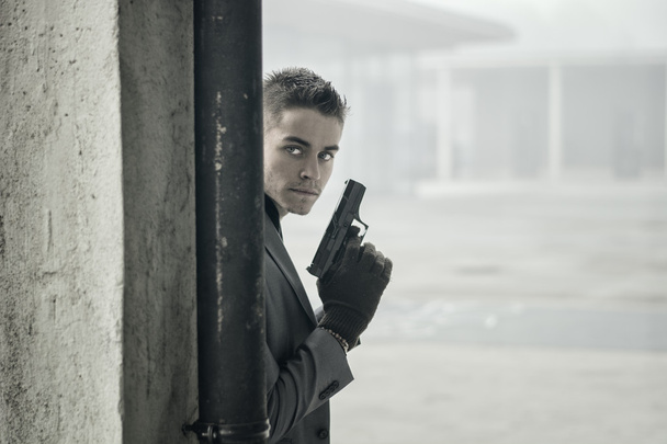 Young detective or policeman or mobster in an urban setting holding a gun - Photo, Image