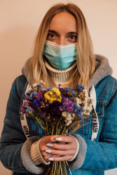 Mladá žena v lékařské masce drží v rukou suché květiny. Kvalitní fotografie - Fotografie, Obrázek
