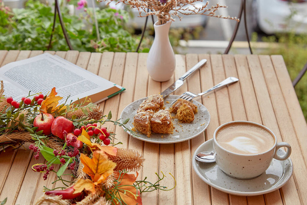 木製のテーブルの上に秋の装飾の中でドーナツとカプチーノをカット-本で外の審美的なコーヒー時間。大気中のコーヒータイム - 写真・画像