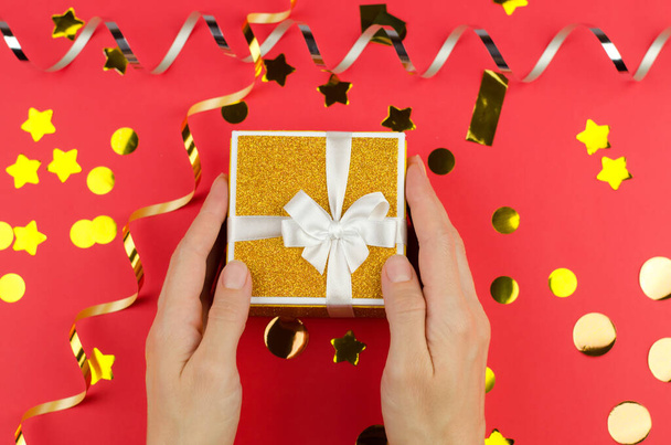 Golden gift box in female hands on a red festive background - Photo, Image