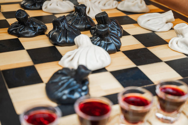 Tradycyjne gruzińskie danie, khinkali Kalakuri, na drewnianym stole, szachownica, rustykalny, widok z boku, czarne i lekkie ciasto, gra w szachy. Selektywne skupienie, widok z boku. Mięso i sery - Zdjęcie, obraz