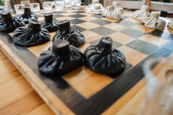 Tradycyjne gruzińskie danie, khinkali Kalakuri, na drewnianym stole, szachownica, rustykalny, widok z boku, czarne i lekkie ciasto, gra w szachy. Selektywne skupienie, widok z boku. Mięso i sery - Zdjęcie, obraz