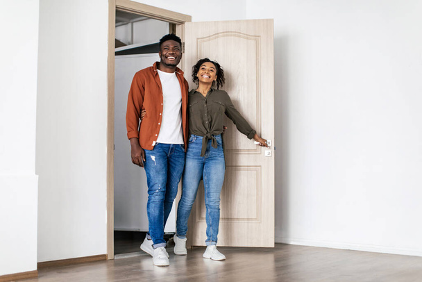 Fröhliche afroamerikanische Ehepartner betreten nach dem Umzug ein neues Zuhause und umarmen sich beim Blick auf das geräumige Wohnzimmer drinnen. Immobilienkäufer Coupe Moving House. Schuss in voller Länge - Foto, Bild