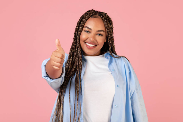 Happy Black Plus Size Lady Gesturing Thumbs Up Sign Smiling To Camera Standing In Studio Over Pink Background. Braided Overweight Woman Approving Something. I Like This Offer Concept - Photo, Image
