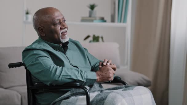 Töprengő álmodozás egyedül nyugalom idős beteg. idős afrikai kopasz férfi szürke szakállal idősebb érett nagyapa ül tolószéken otthon nézi félre álmok gondolkodás elmélkedik mélyen az emlékek Alzheimer beteg - Felvétel, videó