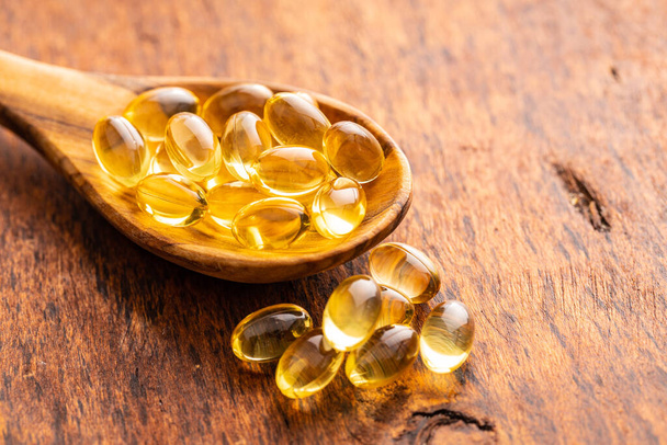 Fish oil capsules. Yellow omega 3 pills in spoon on the wooden table. - Foto, afbeelding