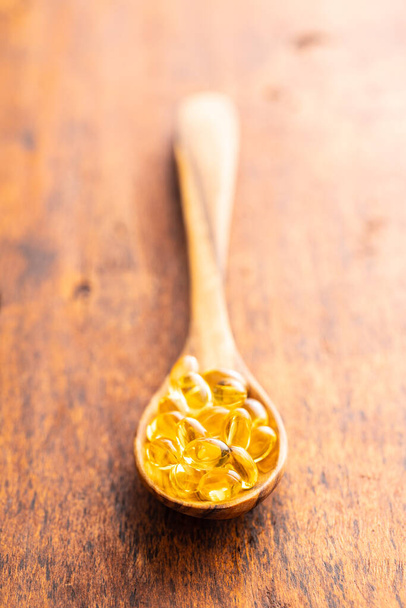 Fish oil capsules. Yellow omega 3 pills in spoon on the wooden table. - Foto, Imagen