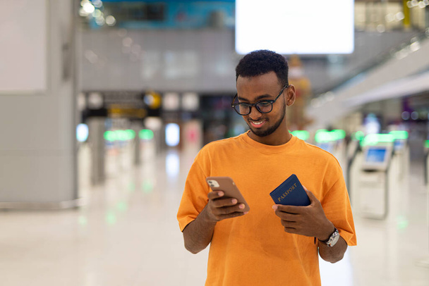 Young handsome black man ready to travel at airport terminal waiting for flight while using phone - Photo, Image