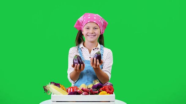 cute, smiling, little farmer girl shows a box with different fresh vegetables, harvest. on green background in studio. Healthy food to your table, Healthy nutrition. High quality photo - Photo, Image