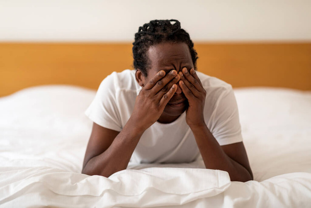 Stanco afroamericano uomo strofinando gli occhi mentre si sveglia a letto dopo la notte insonne, Millennial Black Guy si sente assonnato, soffrendo di mal di testa mentre sdraiato in camera da letto a casa, primo piano con spazio libero - Foto, immagini