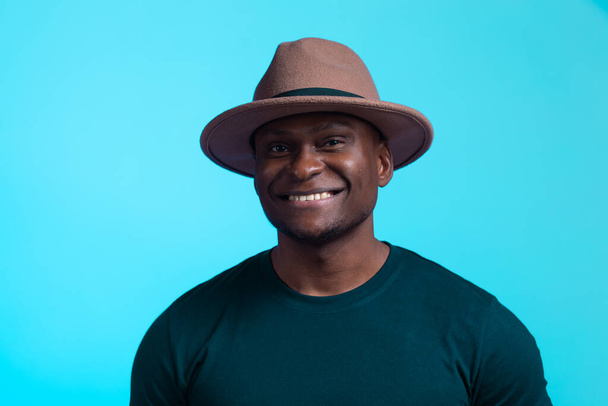 Усміхнений щасливий американський африканський чоловік носить стильний капелюх на рожевому та фіолетовому тлі. Святкова і вечірка
 - Фото, зображення