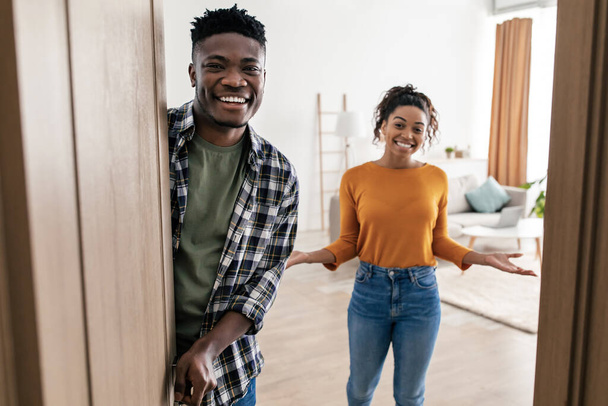 Welcome. Joyful Black Spouses Opening Door Smiling To Camera Meeting You Posing Standing At Home. Family Welcoming You To New House. Real Estate Ownership. Selective Focus - Photo, Image