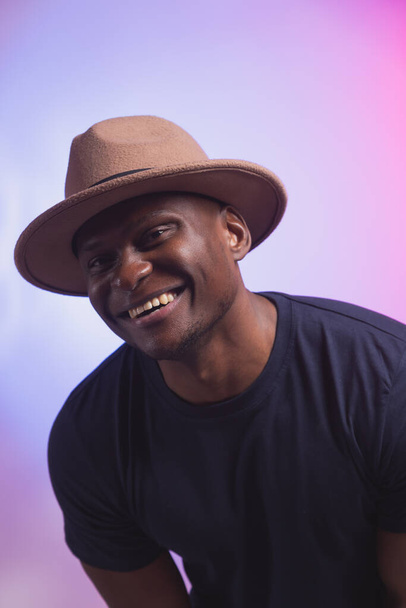 Усміхнений щасливий американський африканський чоловік носить стильний капелюх на рожевому та фіолетовому тлі. Святкова і вечірка
 - Фото, зображення