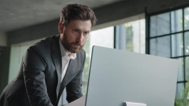 Caucasian busy bearded man adult 40s businessman employer standing in office has problem with paperwork typing data computer online check report contract work with papers and online corporate service - Footage, Video