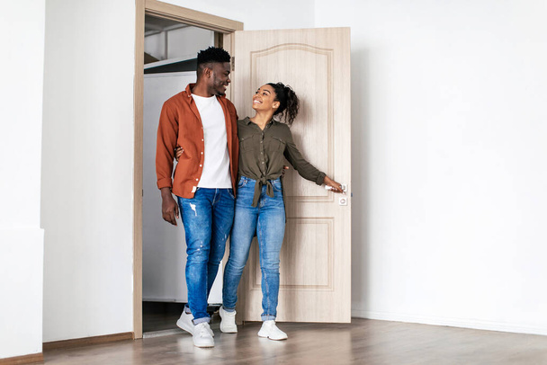 Новий дім. Щасливий чорний чоловік і дружина стукають у власний будинок, позуючи у відкриті двері. Покупці нерухомості переїжджають в квартиру. Концепція релокації. Повнометражний знімок
 - Фото, зображення