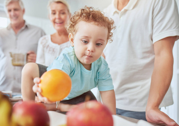 Health, family and baby with orange nutrition for healthy diet, vitamins and minerals on kitchen table at home. Food, fruit and apples for cute child growth and wellness with grandparents and parent - Photo, Image