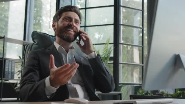 Valkoihoinen iloinen parrakas mies pomo johtaja myyntimies työntekijä agentti sijoittaja asianajaja 40s liikemies istuu toimistossa puhuminen puhelin ystävällinen keskustelu älypuhelin keskustella yrityksen projekti - Materiaali, video