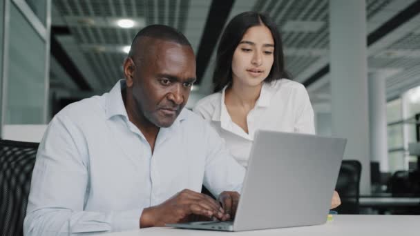Αραβίδα εκπαιδευτής ηγέτης γυναίκα βοηθήσει αφρικανός συνάδελφος άνθρωπος με την εργασία του υπολογιστή επιθεωρήσει εκπαιδευόμενος ελέγχουν τα λάθη στο laptop. Δύο επιχειρηματίες συζητούν το εταιρικό λογισμικό του έργου σε ομαδική εργασία στο γραφείο - Πλάνα, βίντεο